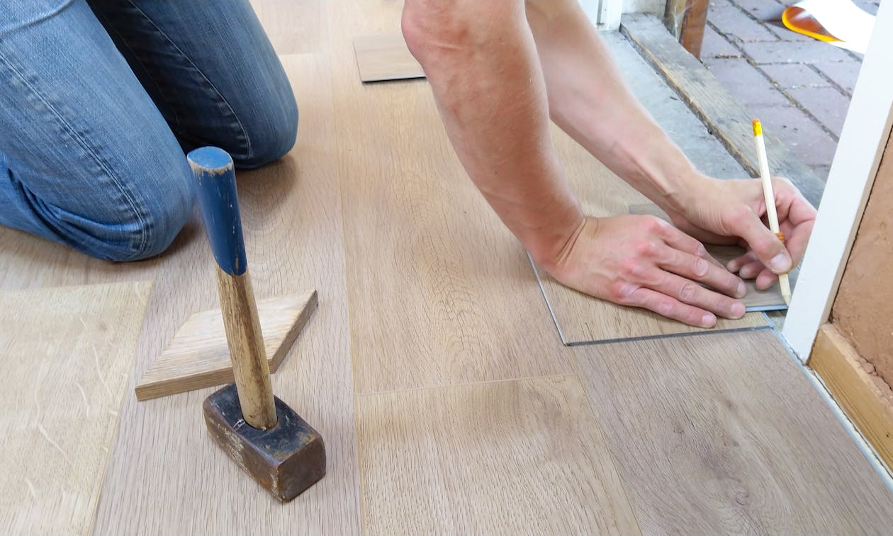 A craftsman carefully measures and marks wooden floor panels for precise installation. — epoxy garage floors near me
