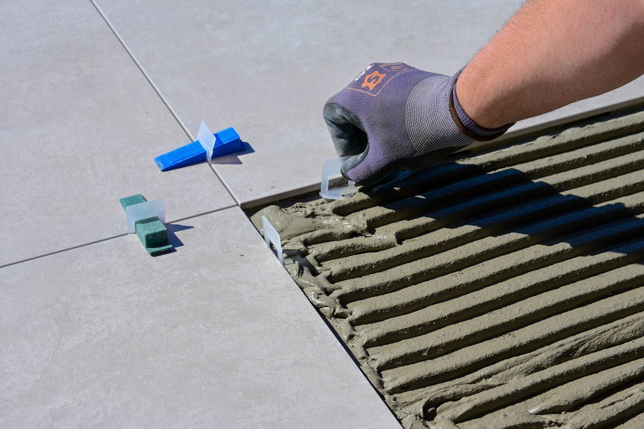 Detailed view of gloved hand aligning tiles with levelers and spacers during construction. — basement floor epoxy coating