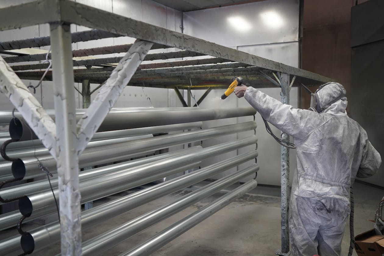 Technician applying powder coating to metal pipes in a workshop setting. — epoxy driveway sealer